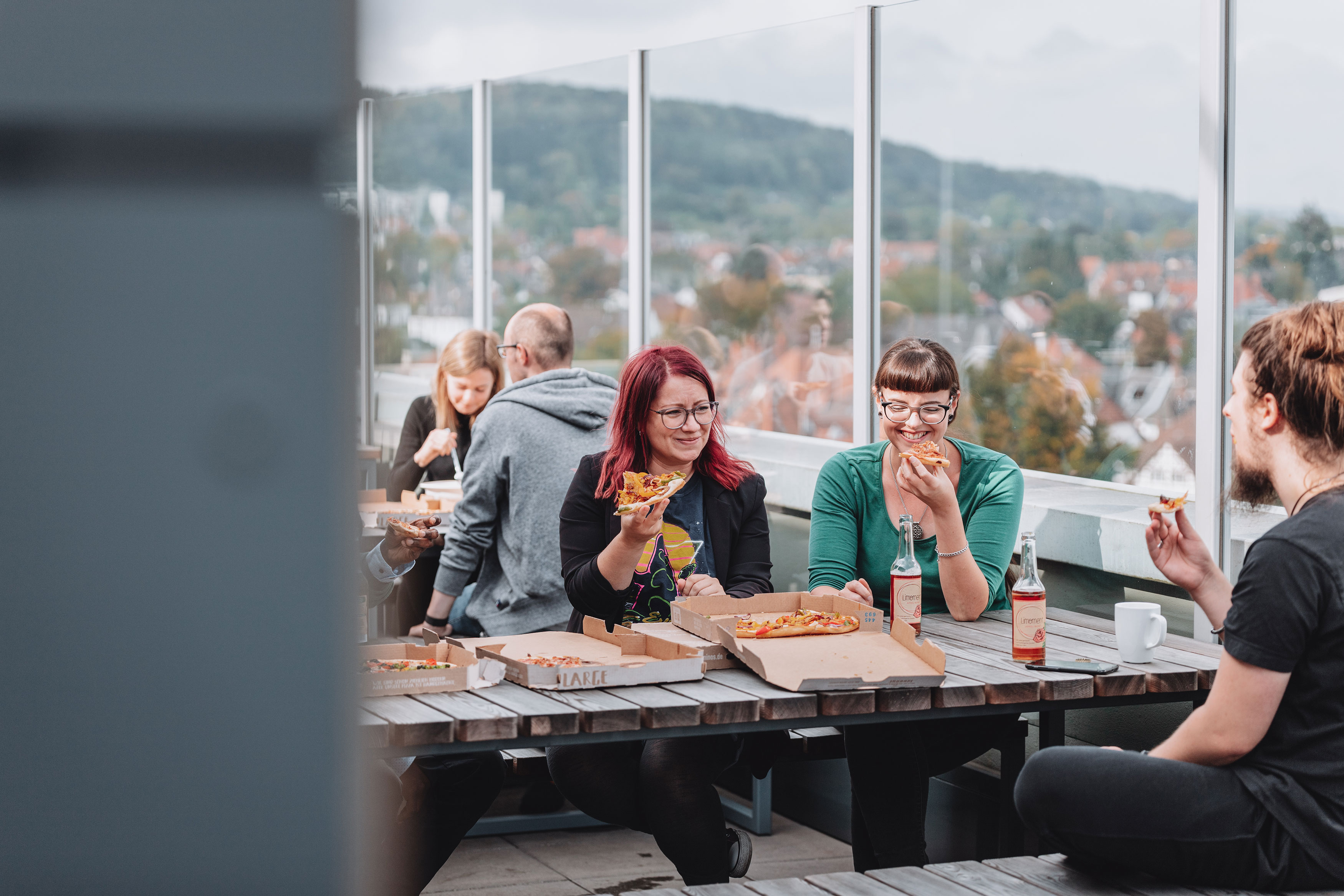 Personen sitzen draußen an größeren Tischen und essen Pizza.