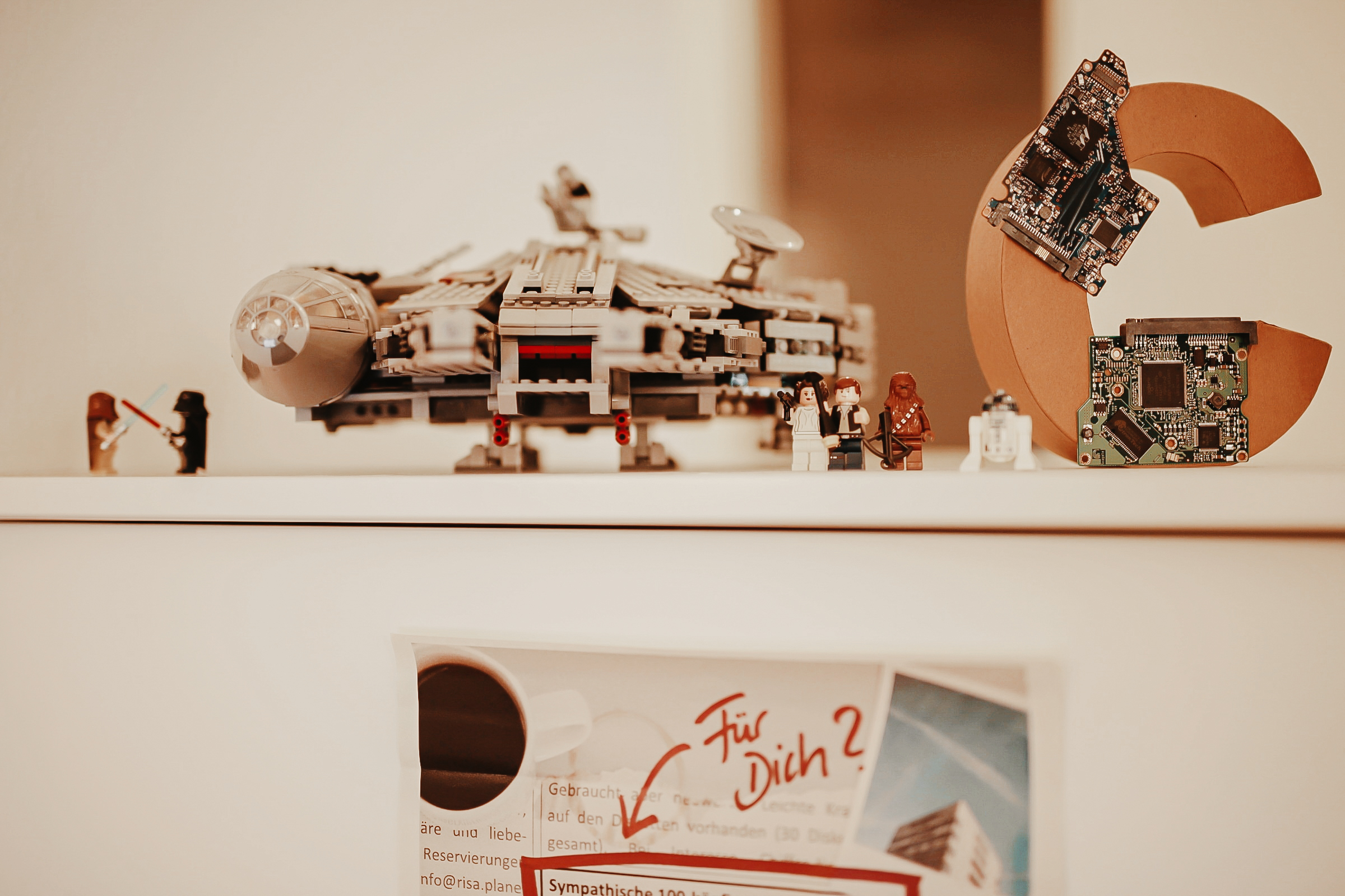 Auf einem Schrank steht ein Playmobil Schiff von Star Wars sowie ein aus Pappe gefertigtes C. davor stehen einige Playmobilfiguren von Star Wars.