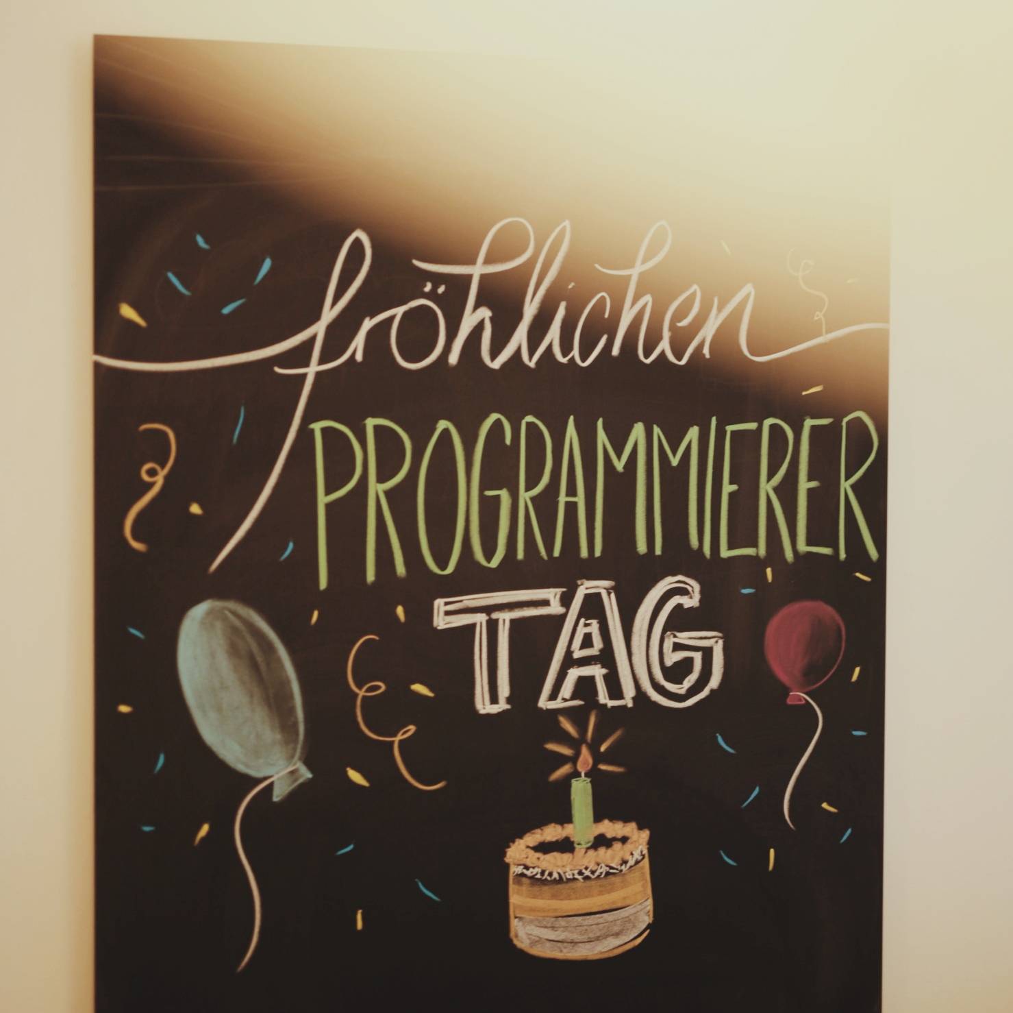 Auf einer großen Tafel steht in bunter Schrift "Fröhlicher Programmierer-Tag"
